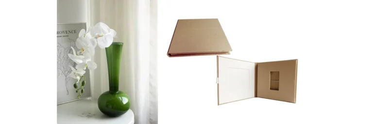 Beige photo album displayed open and closed next to a green vase with white orchids on a white surface.