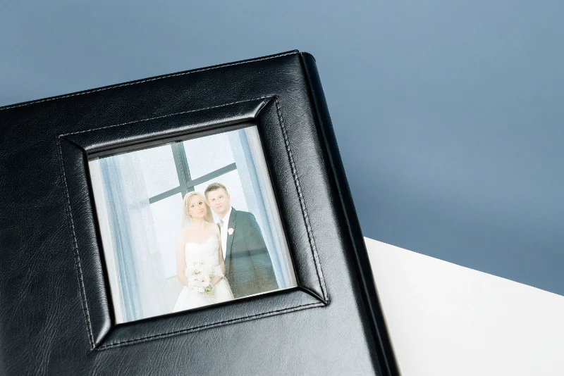 A close-up shot of a leather-bound wedding album cover with a window showing a couple's photo