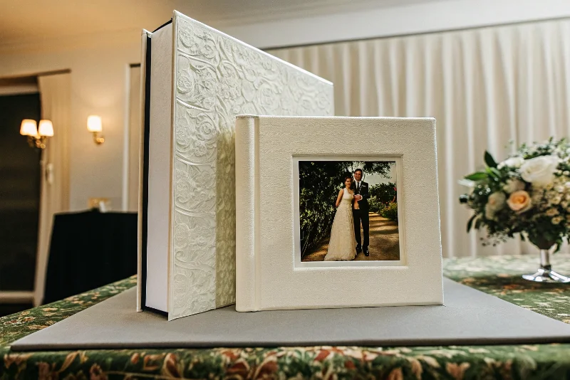 A luxurious white wedding album with a photo window, open on a decorated table