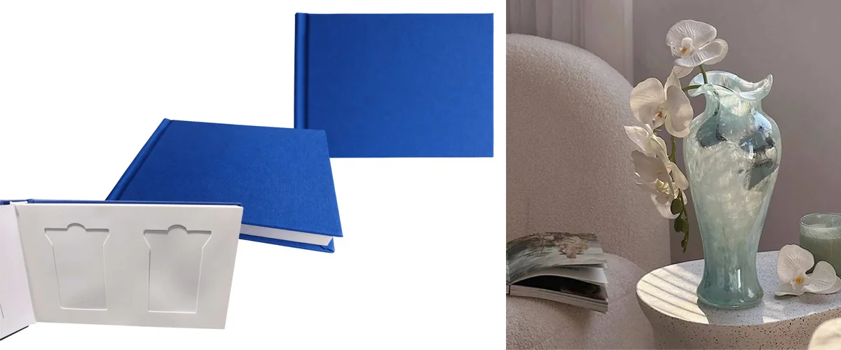 Two blue hardcover photo albums with blank inserts alongside a turquoise decorative vase with white orchids on a minimalist table.
