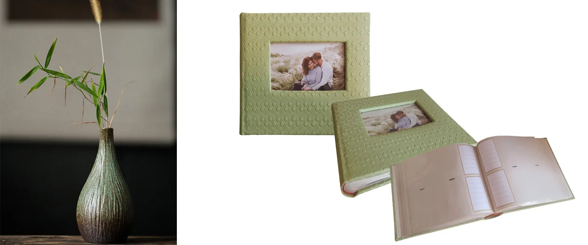 Two light green decorative photo albums with textured covers and a floral vase holding bamboo stems on a table.