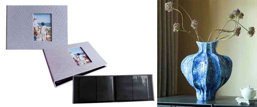 Two textured photo albums with cover frames showing family photos placed next to a glossy decorative blue vase holding dried flowers.