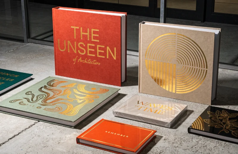 A collection of coffee table albums in different trendy colors&mdash;like sage green, terracotta, and beige&mdash;with custom gold foil text.