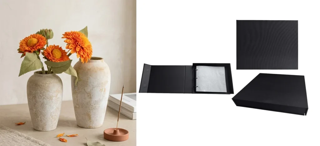 Two ceramic vases with orange flowers next to a sleek black photo album with an open and closed display on a minimalistic surface.
